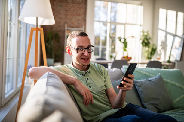 istock Smiling young man on couch with smartphone, daytime 2186458778