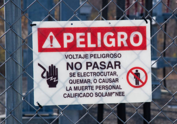 A sign in Spanish warning against electrocution and danger hanging on a chain link fence
