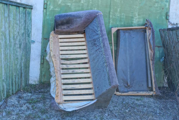 one old broken grey brown two piece sofa stands against green wall in rural street