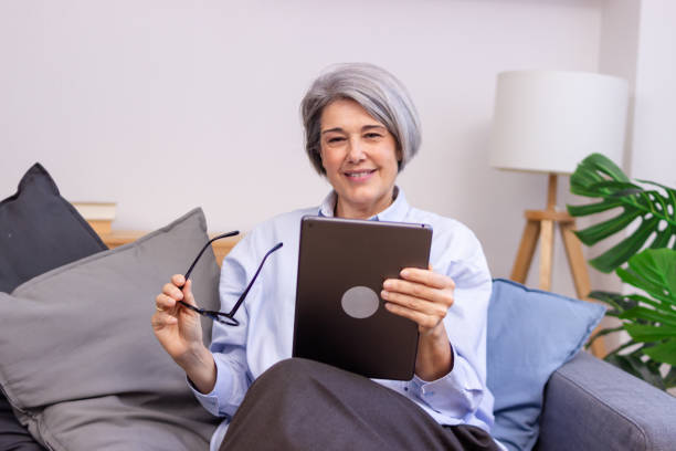 istock Smiling senior woman using digital tablet on sofa at home 2186489104