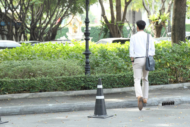 The 40-year-old Asian businessman walking in the parking lot during the daytime.
