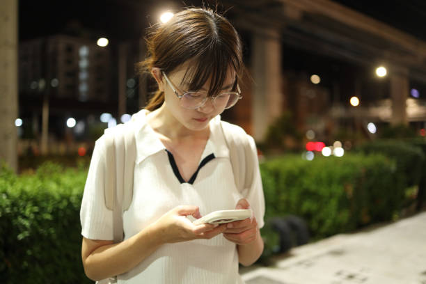 The young East Asian woman using a smartphone in the city at night.