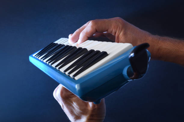 Man prepared to play melodica in hands with blue background illuminated with white light beam.