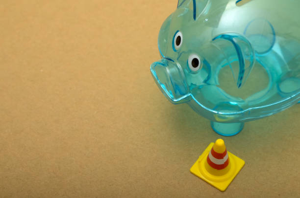 Stock photo showing close-up view of a coin filled baby feeding bottle with silicone teat (nipple) and blue cap ring besides a blue baby dummy (pacifier) against a blue background. Male coded childcare baby raising cost concept.