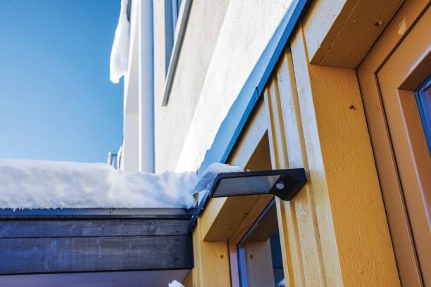 istock LED light fixture with motion sensor mounted on yellow wooden wall villa, covered by snow, under clear blue sky. Sweden. 2186498813