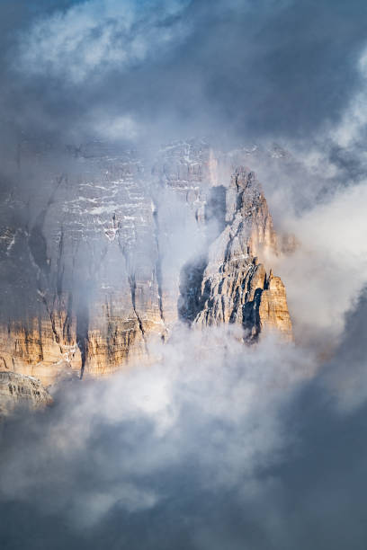mountains in the dolomites behind bad weather clouds and fog, first snow on the rocks during late autumn season