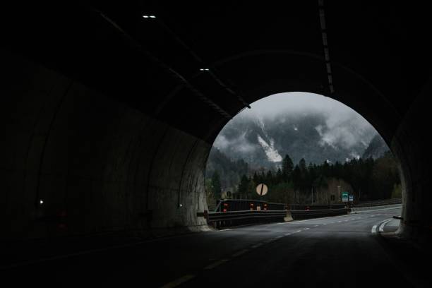 istock View from inside a dark tunnel looking out towards misty mountains and a forest road 2186508328