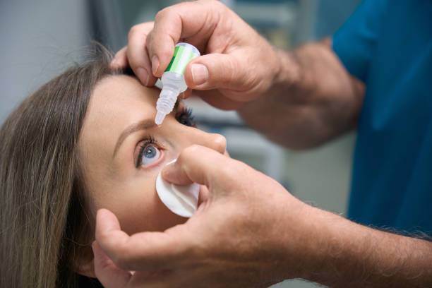 Male optometrist putting eye drops in eyes of young woman for clear vision in clinic stock photo
