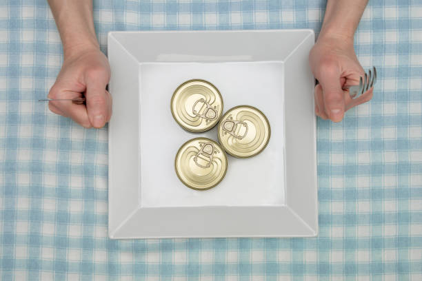 person at table with canned food on empty dish