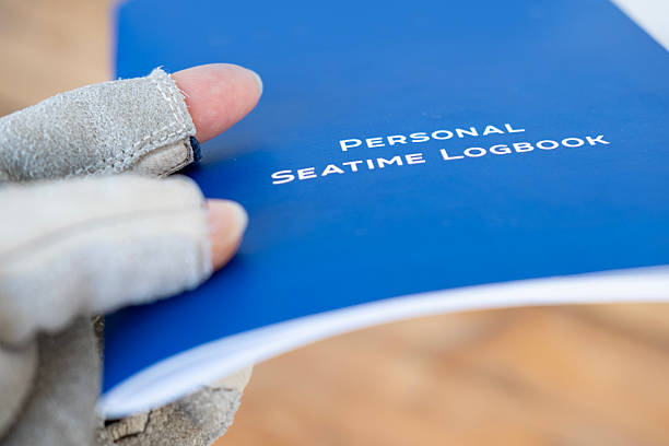 istock Gloved hand holding blue Personal Seatime Logbook. Maritime record keeping. Seafarer documentation. Nautical career tracking, Seafarer's chronicle, Sea hours documented 2186517291