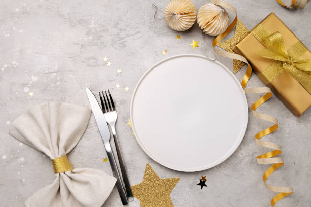 istock Christmas or holiday table with gift box an empty white plate, elegant cutlery and golden decor serpentine stars gift box 2186518059