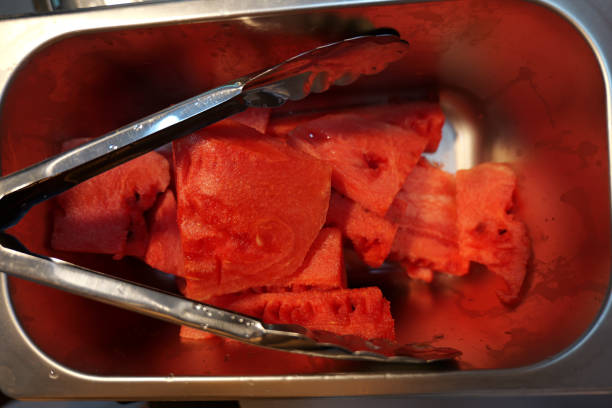 Freshly cut watermelon slices ready to serve in a stainless steel container.