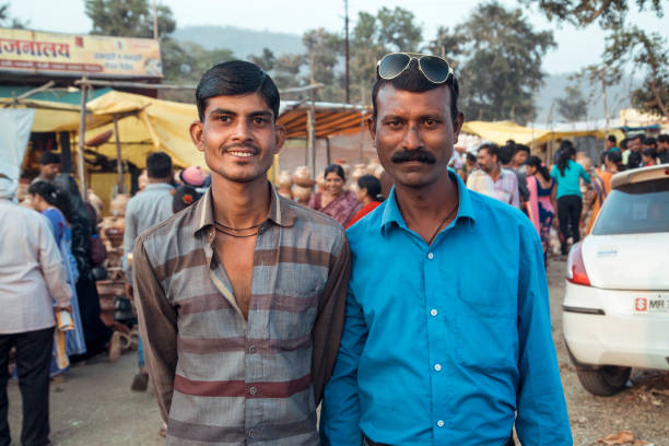 Paratwada Region, India - Two men stand side by side, smiling at the camera, in a lively market setting amidst the rural beauty of Maharashtra during a sunny day.