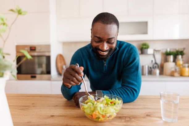 istock Man enjoying salad at wooden table in bright modern kitchen 2186531807