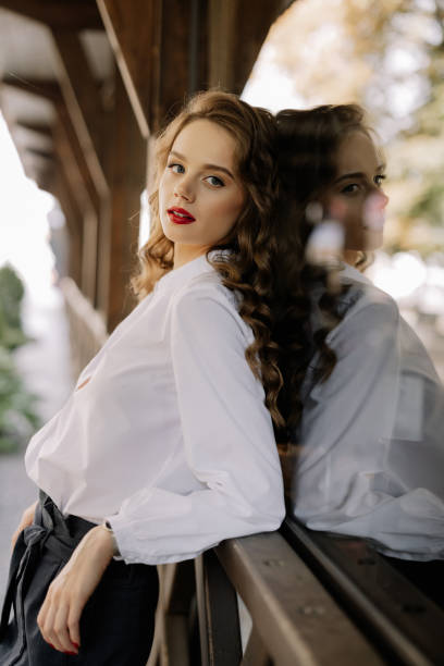 Businesswoman with red lipstick and long brown curly hair leaning on railing with reflection in window