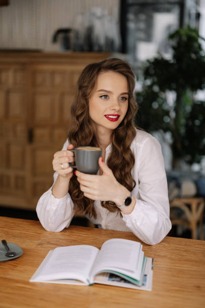 istock Young woman drinking coffee and reading book in cafe 2186537857