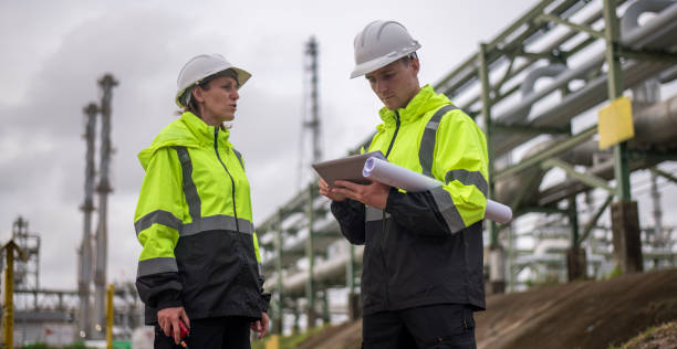 istock Engineers wearing safety gear, including hard hats examining survey a large blueprint tablet standing industrial facility gas or oil refinery engaged in a job requires high safety standards concept 2186572162