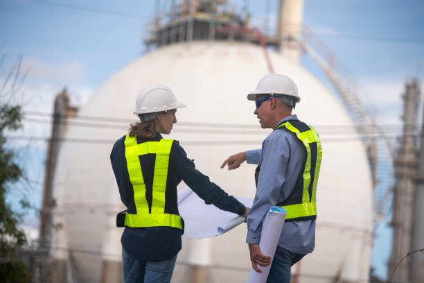 istock Engineers wearing safety gear, including hard hats examining survey a large blueprint tablet standing industrial facility gas or oil refinery engaged in a job requires high safety standards concept 2186572416