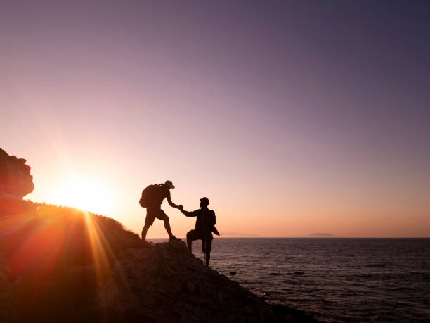 istock Hikers helping each other to climb a rock at sunset 2186575116