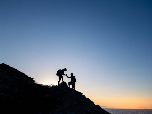 istock Hikers helping each other to climb a mountain at sunset 2186575117
