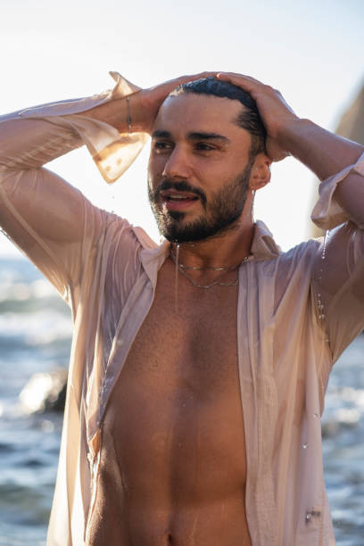 Young man with toned abs drying his hair in the sun after swimming. Perfect summer beach vibes with fit body and natural beauty