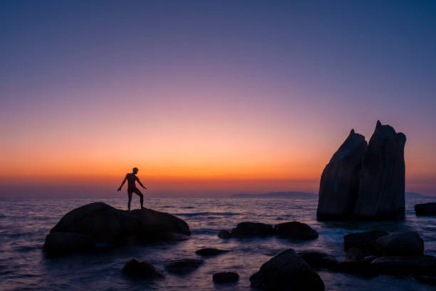 istock Young man balancing on rock at sunset on the beach 2186575175