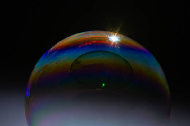 A bubble is floating in the air with a green and purple hue. The bubble is surrounded by a blurry background of grass and dirt