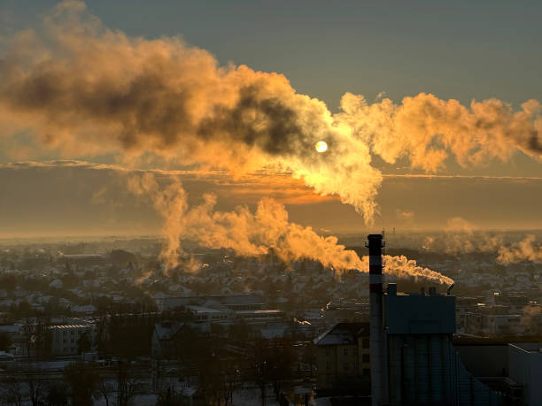 Smoking industrial smoke stacks in winter time against sunlight