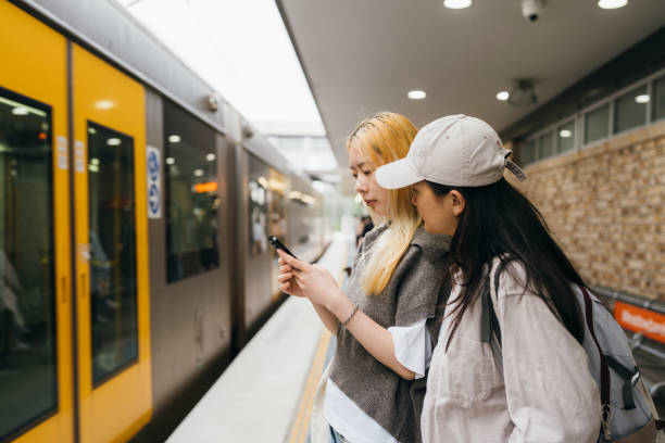 istock Friends standing on a platform beside a yellow train, focused on a phone 2186587956