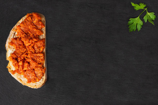 Slice of bread with Mallorcan sobrasada on a black stone plate.