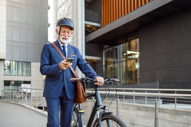 istock Confident bearded senior businessman messaging over smart phone while pushing his bicycle in city 2186599835