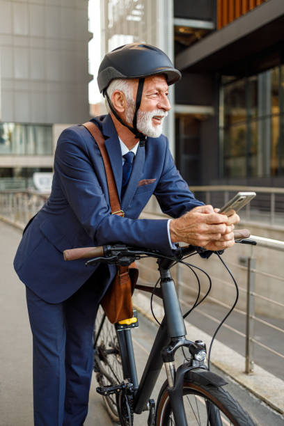 istock Thoughtful male professional in helmet using phone and looking away while leaning on bicycle in city 2186599836
