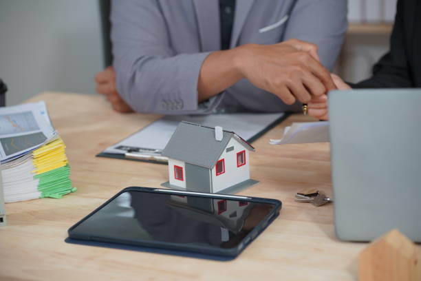 istock Real estate agent holding house model and pen discussing contract terms with client, making agreement with real estate agent, concept for home insurance consultant 2186603254