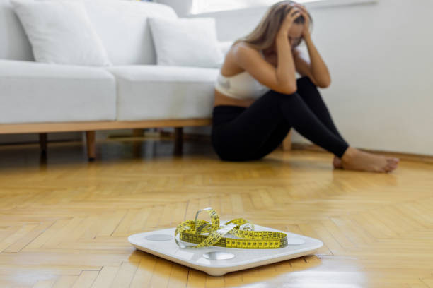 Upset and sad woman with measuring tape on wooden floor