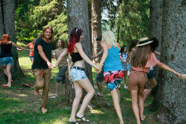 Young people dancing around and hugging trees. Large group of young people in forest.