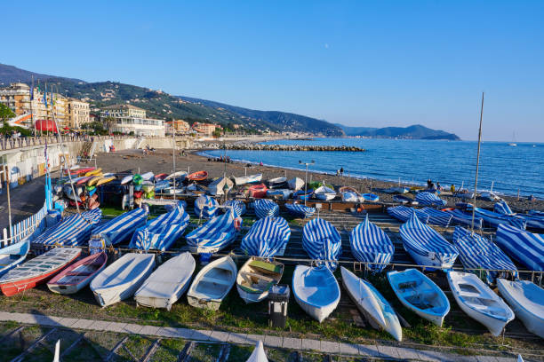 Lavagna, Italy - November 10, 2024: tourists relaxing on the beach on a sunny afternoon of November. In the foreground several small fishing boats moored for the winter season.