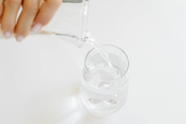 Unrecognizable female pouring clean drinking water from jug into glass
