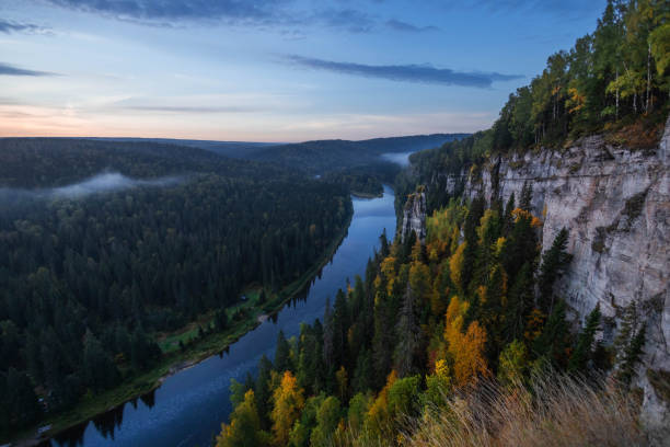 istock A tranquil river flows gently through lush green forests and towering cliffs at dusk, with mist rising above the water and vibrant autumn foliage illuminating the scene 2186633037