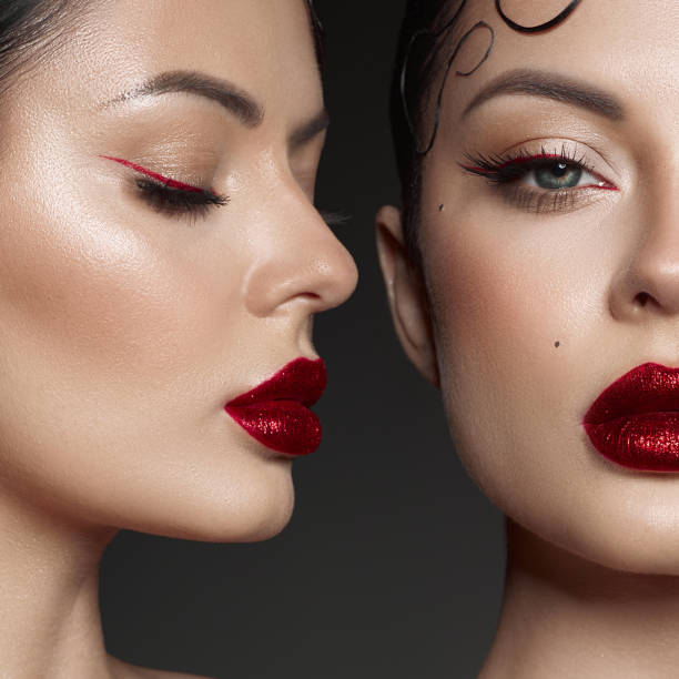 Two models present a fashion-focused beauty display highlighting intricate makeup techniques, featuring vibrant red lips and precise eyeliner against a dark backdrop