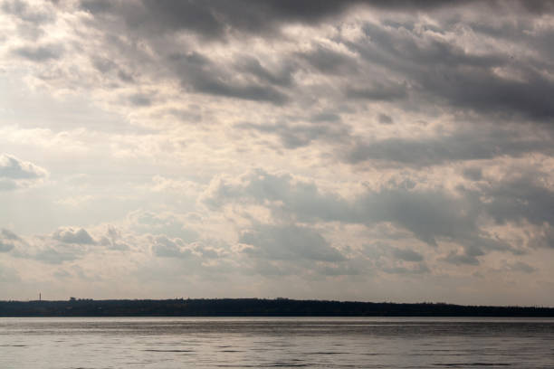 a dark ocean with a cloudy sky and the sun shining through the clouds.