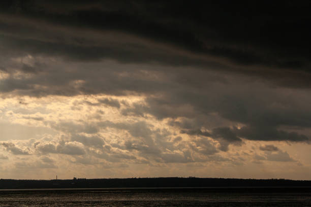 a dark ocean with a cloudy sky and the sun shining through the clouds.