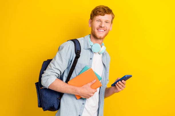 istock Photo of cheerful positive boy hand arm hold telephone backpack planner diary ready learning isolated on yellow color background 2186640817