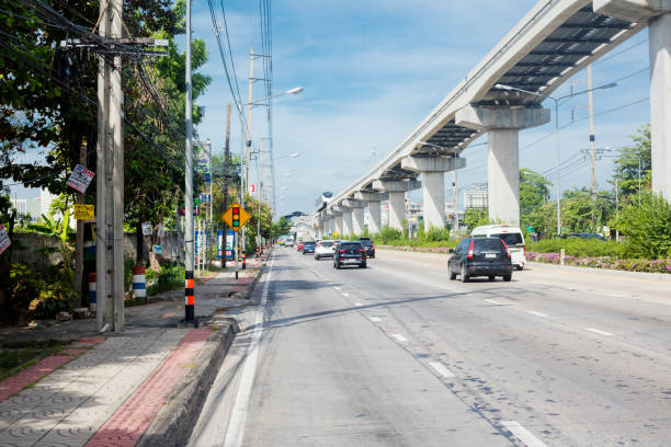 View along Ramintra Road with traffic and new elevated BTS LRT train passing on tracks from east to west.  View is from east to west. On street traffic is ruling on Ramintra Road in Bangkok Ramintra. In far background is next BTS station Ram Intra Kor Mor 6