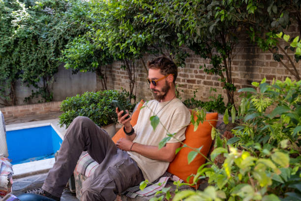 istock Young man relaxing by the pool, browsing his smartphone in a peaceful garden 2186649688