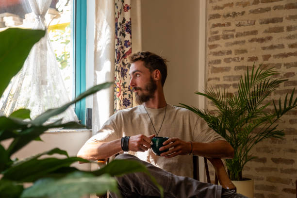 istock Young man relaxing at home, drinking tea and looking out the window 2186649797