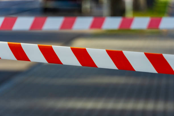 istock Caution tape with bright red and white stripes is stretched across a pathway in a city, indicating a warning and restricting access to a certain area during the day 2186659536