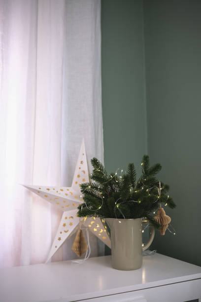 istock A beautifully festive arrangement that features a star, pine branches, and warm, inviting lights all around on white table. 2186661029