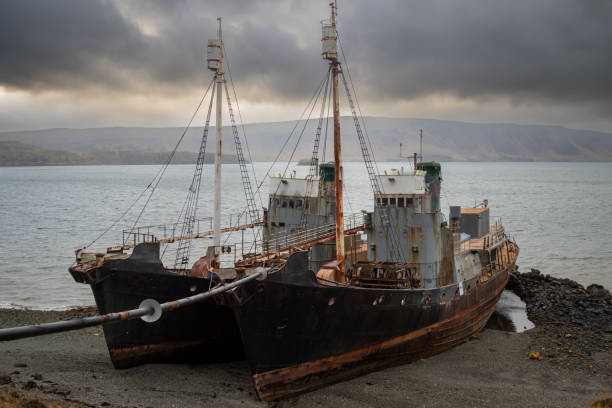 Two old beached whalers on a coast of a fjord. Mountains in the background. Intense cloudy sky. Hvalfjordur, west Iceland.