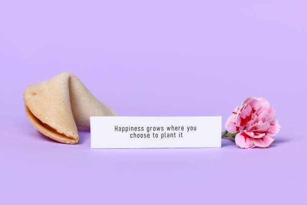 Fortune cookie with motivational text on paper saying 'Happiness grows where you choose to plant it' on violet background with flower