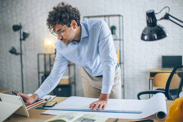 istock Architect concentrating on paperwork, managing projects and working remotely in a bright home office 2186666479